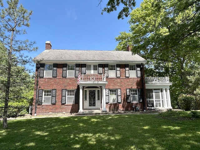 georgian-style home with a balcony, a chimney, a front lawn, brick siding, and a sunroom