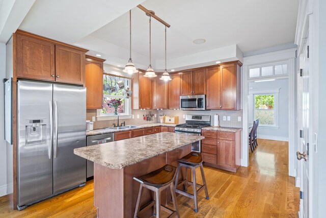 kitchen with appliances with stainless steel finishes, a sink, light wood-style flooring, and tasteful backsplash