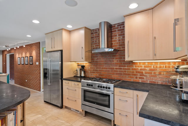 kitchen featuring appliances with stainless steel finishes, wall chimney range hood, dark countertops, light brown cabinetry, and track lighting