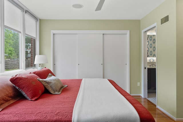 bedroom featuring wood finished floors, a closet, ensuite bath, ceiling fan, and baseboards