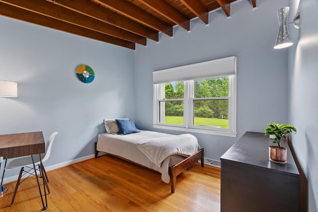 bedroom featuring beam ceiling, light wood finished floors, wooden ceiling, and baseboards
