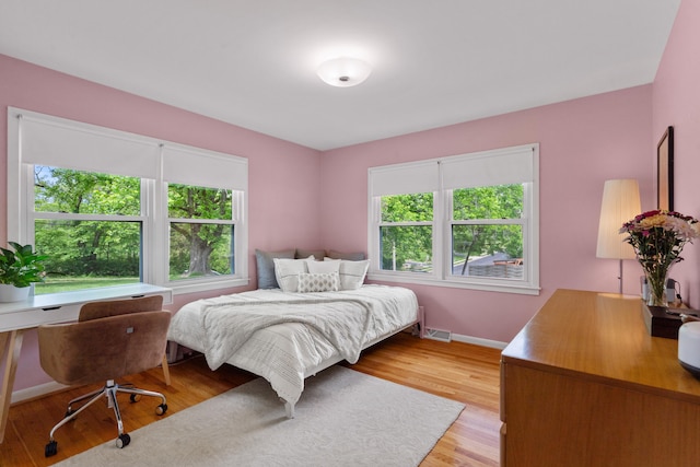 bedroom with light wood finished floors, an office area, and baseboards