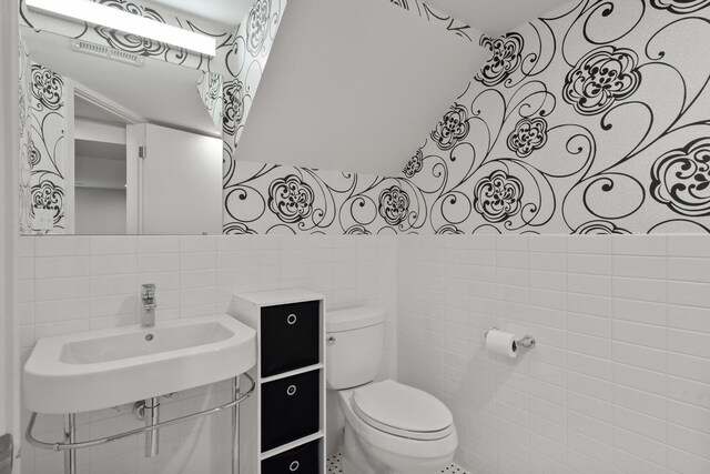 half bath featuring tile walls, toilet, and a sink