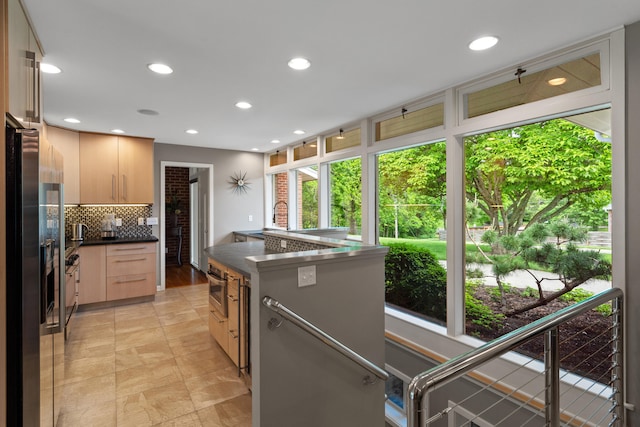 kitchen featuring decorative backsplash, dark countertops, appliances with stainless steel finishes, light brown cabinets, and a sink