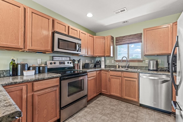 kitchen with appliances with stainless steel finishes, a sink, dark stone counters, and recessed lighting