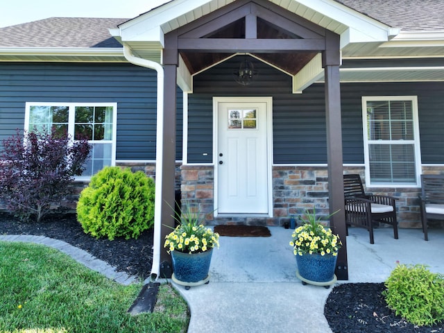 entrance to property featuring covered porch, a shingled roof, and stone siding