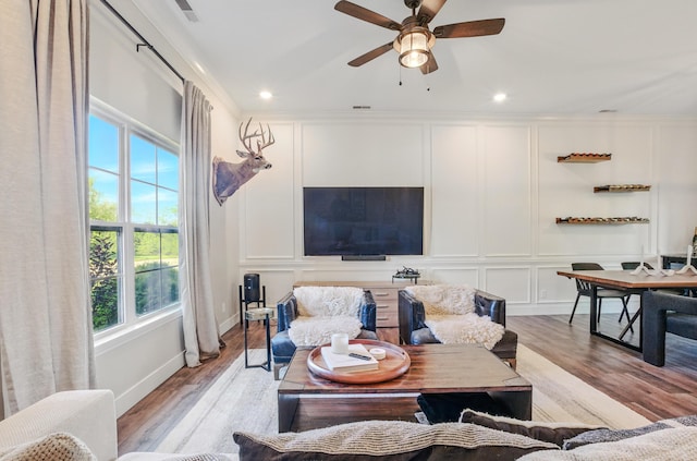 living room with a decorative wall, plenty of natural light, light wood-style flooring, ornamental molding, and a ceiling fan