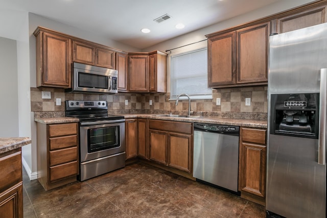 kitchen with stainless steel appliances, a sink, backsplash, brown cabinets, and recessed lighting