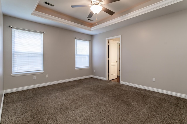 empty room featuring a raised ceiling, dark carpet, ceiling fan, baseboards, and ornamental molding