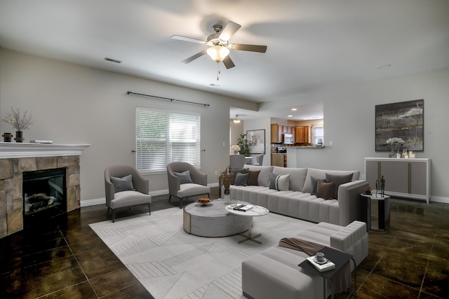 living area with ceiling fan, a stone fireplace, and baseboards