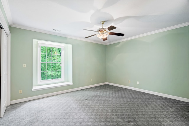carpeted spare room featuring ornamental molding, baseboards, and a ceiling fan