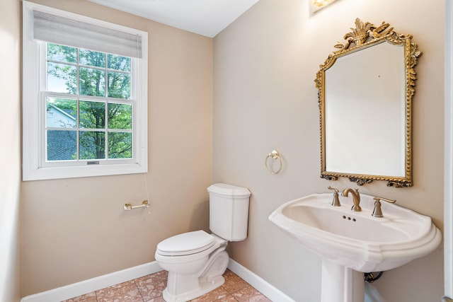 half bathroom with baseboards, toilet, tile patterned floors, and a sink