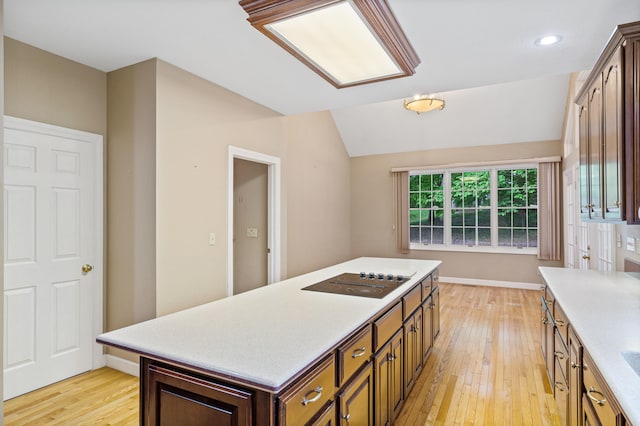 kitchen with black electric stovetop, light wood-type flooring, light countertops, a center island, and vaulted ceiling