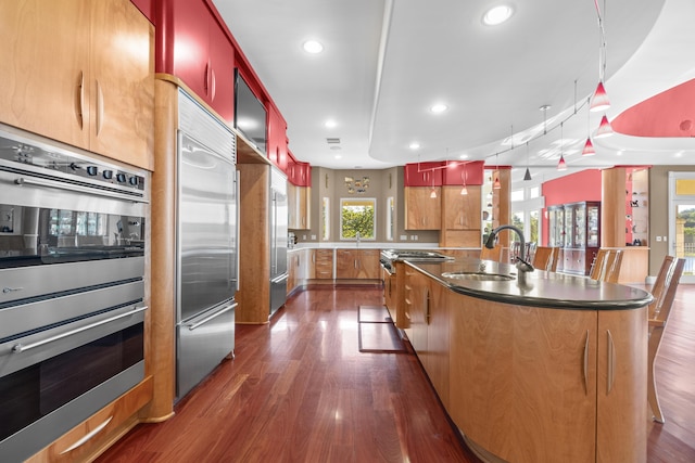 kitchen with a sink, premium appliances, dark wood-style flooring, a large island with sink, and recessed lighting
