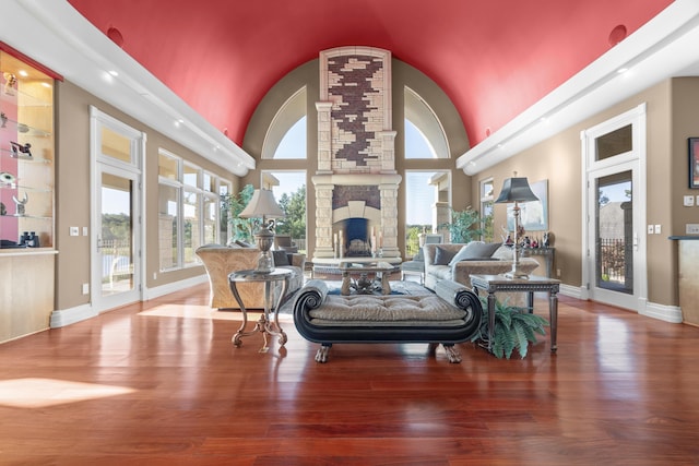 living room with a stone fireplace, a high ceiling, wood finished floors, and baseboards