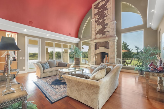living area featuring a towering ceiling, wood finished floors, a fireplace, recessed lighting, and baseboards