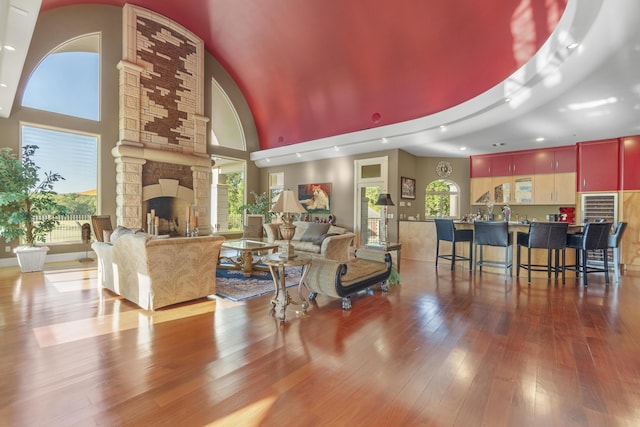 living room with a high ceiling, a stone fireplace, hardwood / wood-style flooring, and recessed lighting