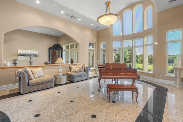 living area with granite tiled floors, recessed lighting, baseboards, a high ceiling, and arched walkways
