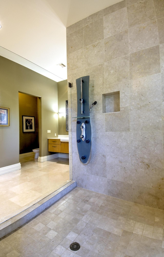bathroom featuring a tile shower, toilet, and vanity