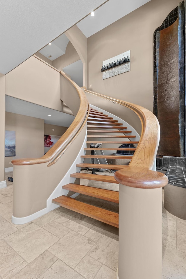 staircase featuring baseboards, stone tile floors, a high ceiling, and recessed lighting