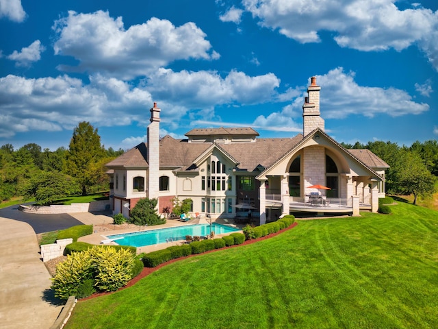 rear view of house featuring a chimney, a lawn, an outdoor pool, and a wooden deck