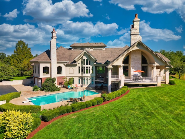 rear view of property featuring a chimney, a lawn, an outdoor pool, a wooden deck, and an attached garage