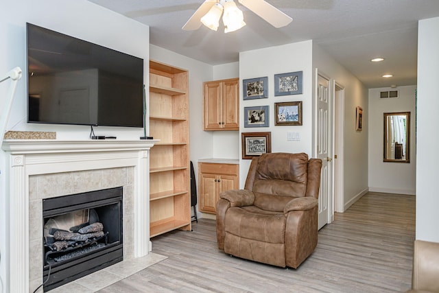 living area featuring a ceiling fan, light wood finished floors, baseboards, a tile fireplace, and recessed lighting