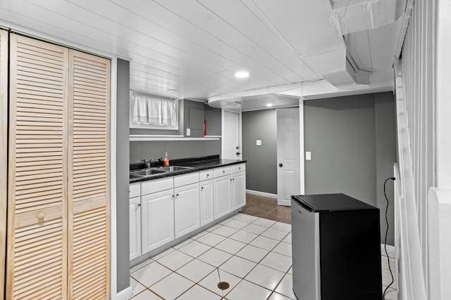 kitchen featuring a sink, refrigerator, dark countertops, light tile patterned flooring, and white cabinetry