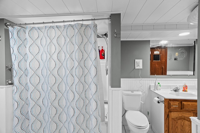 bathroom with vanity, toilet, wainscoting, a decorative wall, and wooden ceiling