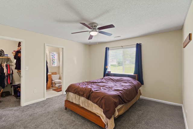 carpeted bedroom featuring a spacious closet, a closet, connected bathroom, a textured ceiling, and a ceiling fan