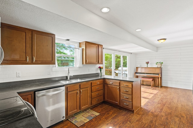 kitchen with stainless steel dishwasher, a sink, a peninsula, dark wood-type flooring, and dark countertops