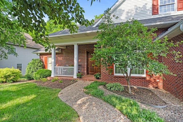 entrance to property with brick siding, a porch, a lawn, and a shingled roof