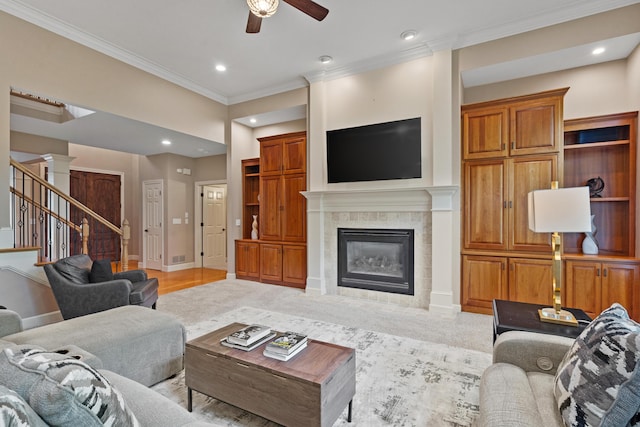 living area featuring ceiling fan, crown molding, a tile fireplace, stairway, and recessed lighting
