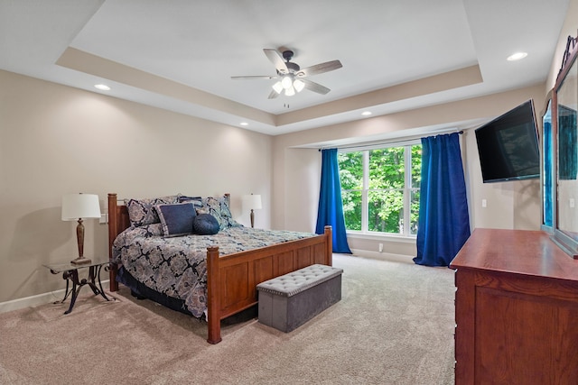 bedroom featuring light carpet, a raised ceiling, baseboards, recessed lighting, and ceiling fan