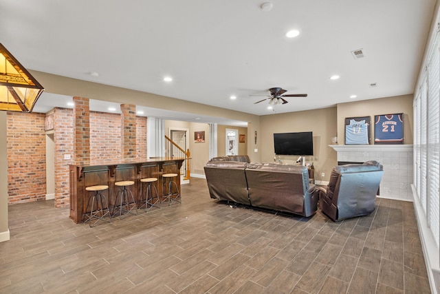 living area with a bar, ceiling fan, wood finished floors, baseboards, and brick wall