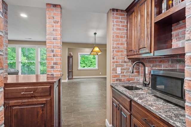 kitchen featuring a sink, stainless steel microwave, baseboards, light stone counters, and wood finished floors