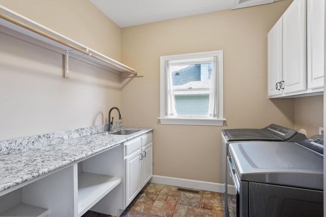 clothes washing area with washing machine and clothes dryer, baseboards, cabinet space, and stone finish flooring