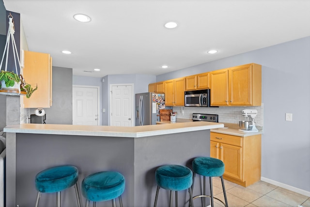 kitchen featuring appliances with stainless steel finishes, a breakfast bar, light tile patterned floors, decorative backsplash, and light countertops