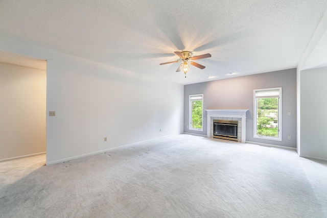 unfurnished living room with ceiling fan, light carpet, a tile fireplace, baseboards, and a textured ceiling