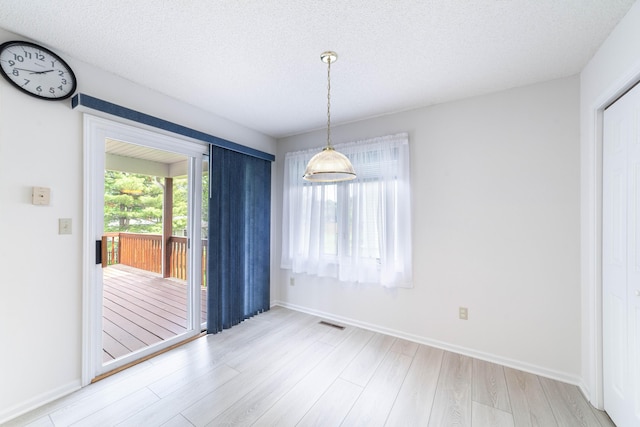 unfurnished dining area featuring light wood finished floors, baseboards, and a textured ceiling