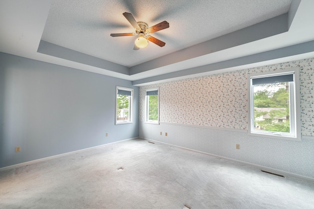 carpeted empty room featuring ceiling fan, wallpapered walls, wainscoting, and a tray ceiling