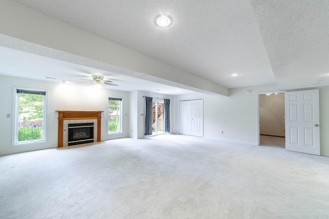 unfurnished living room featuring a tiled fireplace, light colored carpet, ceiling fan, a textured ceiling, and baseboards