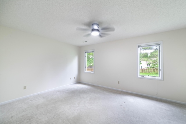 empty room with light carpet, a ceiling fan, baseboards, and a textured ceiling