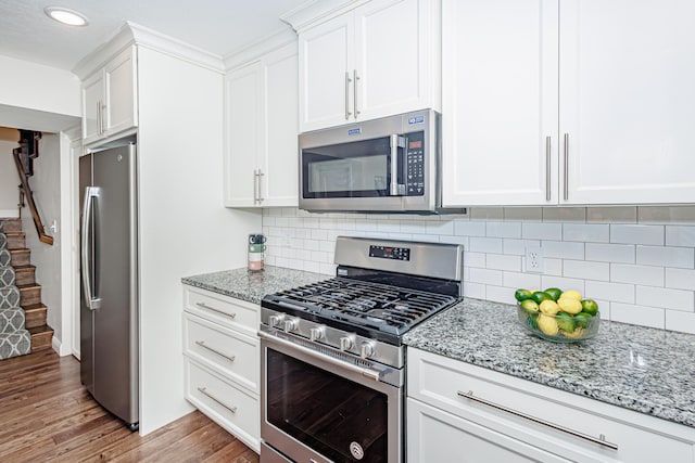 kitchen with stainless steel appliances, light wood-style floors, white cabinetry, light stone counters, and decorative backsplash