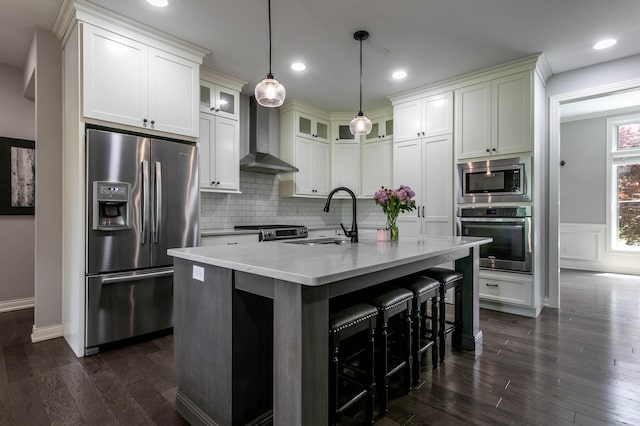 kitchen featuring stainless steel appliances, a sink, wall chimney range hood, decorative backsplash, and dark wood finished floors