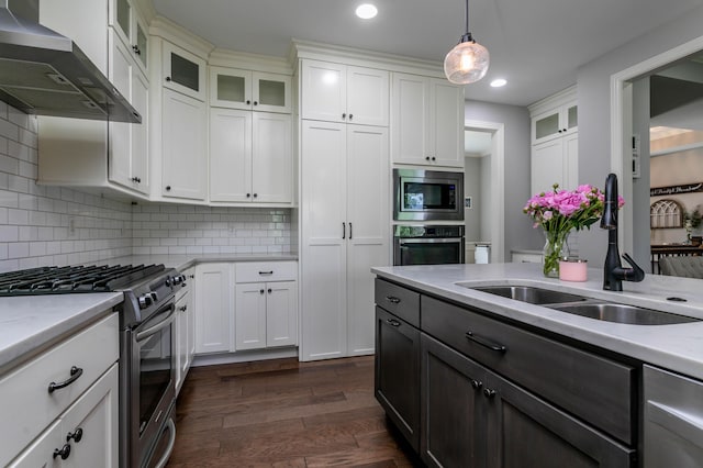 kitchen featuring appliances with stainless steel finishes, a sink, wall chimney exhaust hood, pendant lighting, and white cabinets