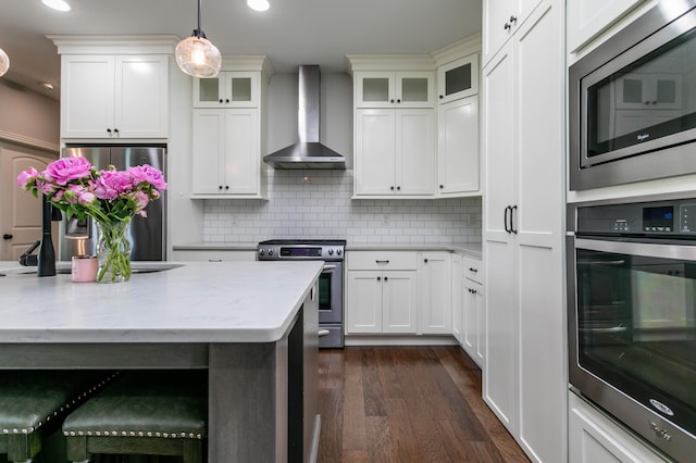 kitchen featuring wall chimney exhaust hood, appliances with stainless steel finishes, dark wood-type flooring, pendant lighting, and tasteful backsplash