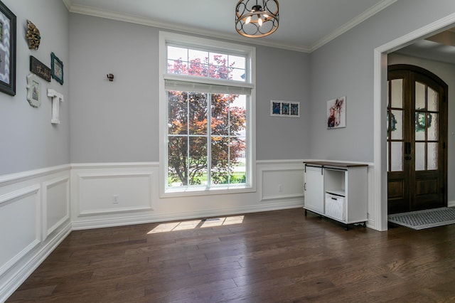 unfurnished dining area with a chandelier, dark wood finished floors, wainscoting, and ornamental molding