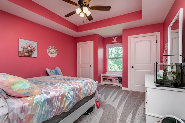 carpeted bedroom featuring a tray ceiling, baseboards, and a ceiling fan