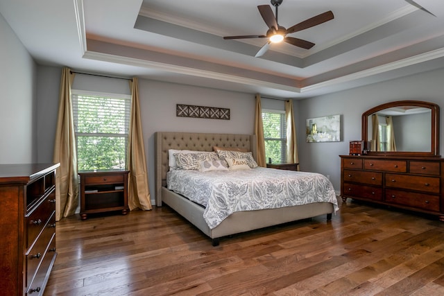 bedroom with a raised ceiling, ornamental molding, dark wood-type flooring, and a ceiling fan
